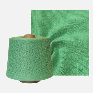 Spool of green yarn next to a swatch of green fabric on a white background